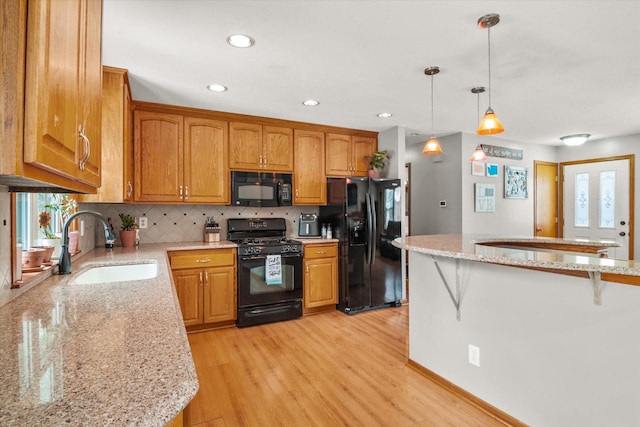 kitchen with a breakfast bar, sink, hanging light fixtures, light hardwood / wood-style floors, and black appliances