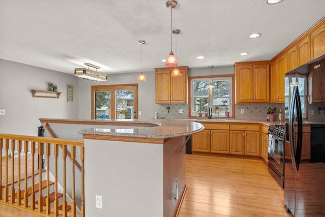 kitchen featuring black appliances, sink, hanging light fixtures, kitchen peninsula, and light wood-type flooring