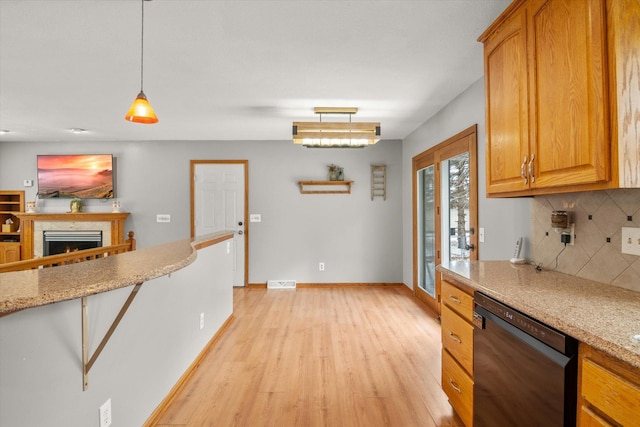 kitchen with pendant lighting, light hardwood / wood-style flooring, backsplash, black dishwasher, and light stone countertops