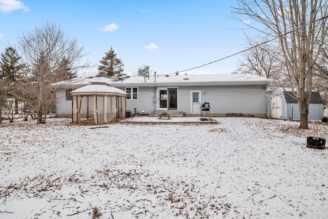 snow covered property featuring a gazebo, a patio, and a storage shed