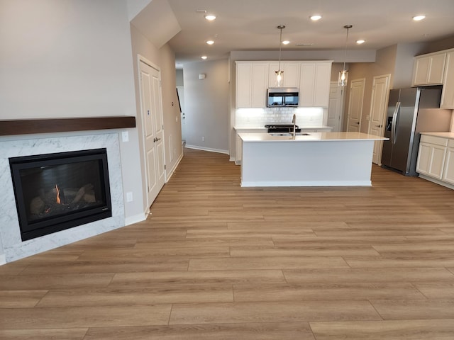 kitchen featuring a center island with sink, hanging light fixtures, appliances with stainless steel finishes, decorative backsplash, and white cabinets