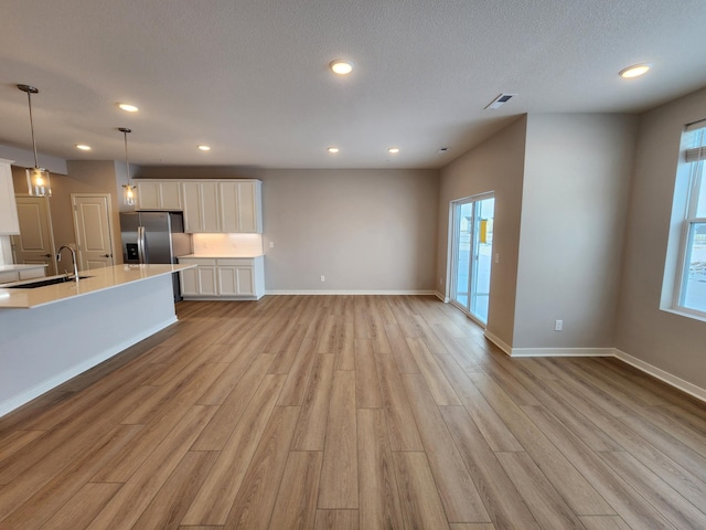 unfurnished living room featuring sink, a textured ceiling, and light hardwood / wood-style flooring