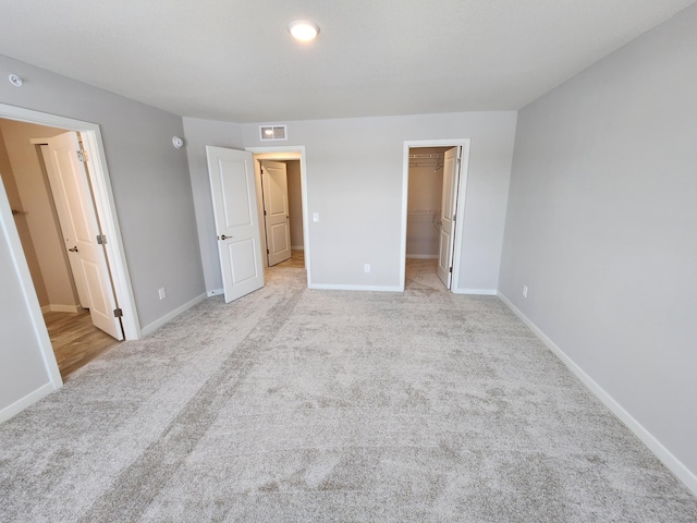 unfurnished bedroom featuring a walk in closet, light carpet, and a closet