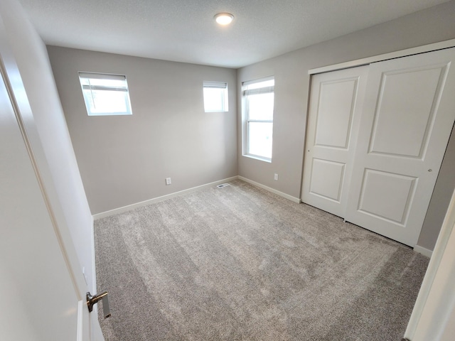 unfurnished bedroom featuring multiple windows, light colored carpet, a closet, and a textured ceiling