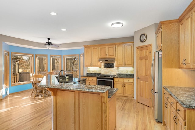 kitchen featuring sink, appliances with stainless steel finishes, a kitchen island with sink, light hardwood / wood-style floors, and dark stone counters