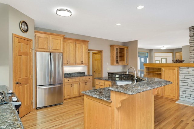 kitchen with stainless steel refrigerator, sink, dark stone countertops, a kitchen breakfast bar, and light wood-type flooring