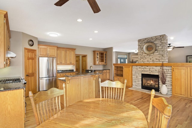 dining room with ceiling fan, a fireplace, sink, and light wood-type flooring