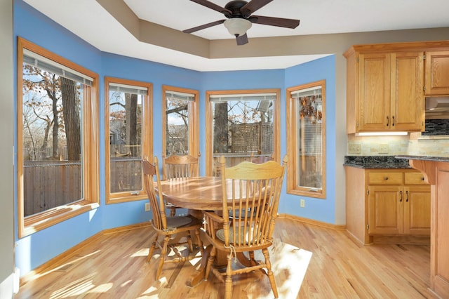 dining space featuring a tray ceiling, ceiling fan, and light hardwood / wood-style flooring