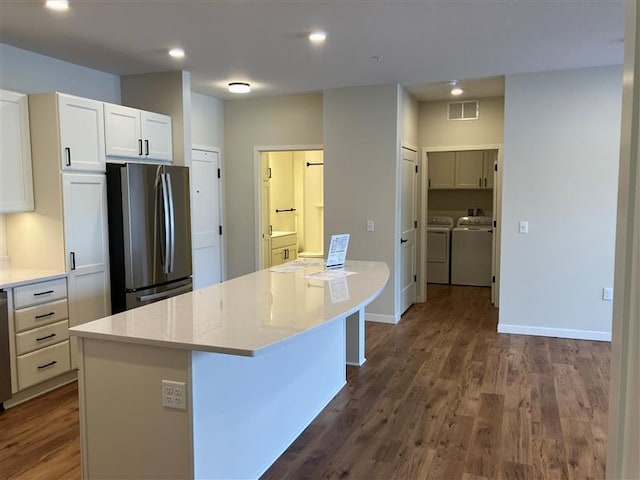 kitchen with a kitchen island, appliances with stainless steel finishes, white cabinetry, washing machine and clothes dryer, and dark wood-type flooring