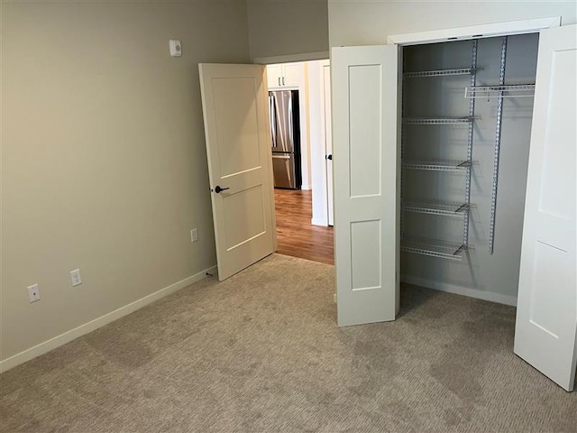 unfurnished bedroom with light carpet, stainless steel fridge, and a closet