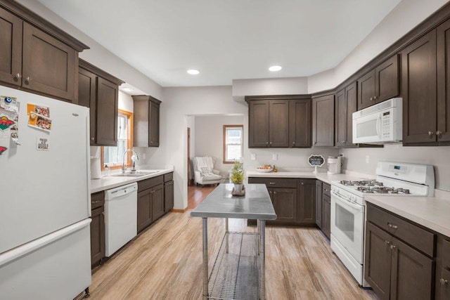 kitchen featuring light wood finished floors, a sink, white appliances, dark brown cabinetry, and light countertops