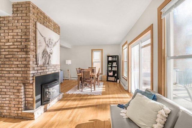 living area with a baseboard radiator, a brick fireplace, and wood finished floors