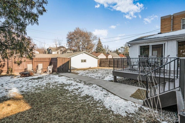 snowy yard featuring a wooden deck, an outdoor fire pit, and fence