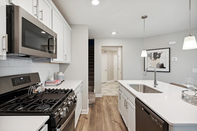 kitchen featuring sink, light hardwood / wood-style flooring, hanging light fixtures, appliances with stainless steel finishes, and white cabinets