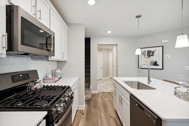 kitchen with sink, appliances with stainless steel finishes, hanging light fixtures, light hardwood / wood-style floors, and white cabinets