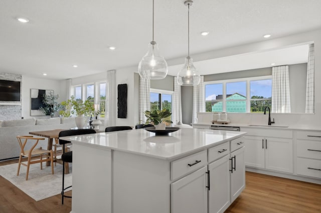 kitchen featuring sink, decorative light fixtures, white cabinetry, and light hardwood / wood-style flooring