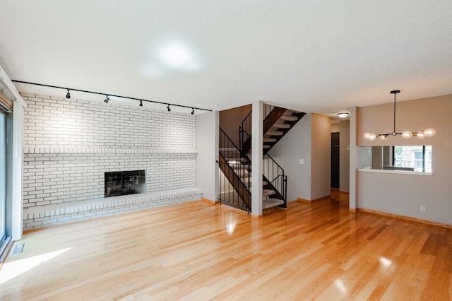 unfurnished living room with hardwood / wood-style flooring, rail lighting, and an inviting chandelier