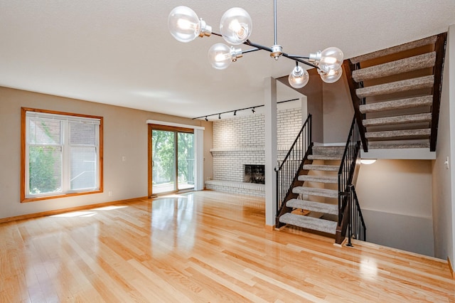 unfurnished living room with a brick fireplace, a notable chandelier, a textured ceiling, and light hardwood / wood-style flooring