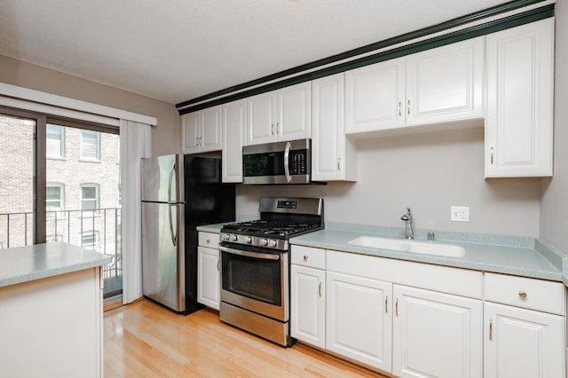 kitchen with sink, light hardwood / wood-style flooring, appliances with stainless steel finishes, a textured ceiling, and white cabinets