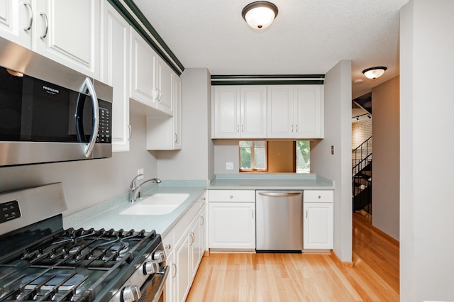 kitchen featuring a textured ceiling, white cabinets, stainless steel appliances, sink, and light wood-type flooring