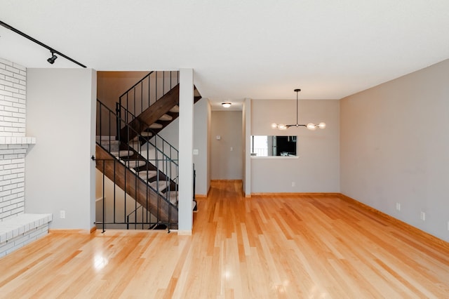 unfurnished living room with a chandelier, track lighting, and hardwood / wood-style flooring