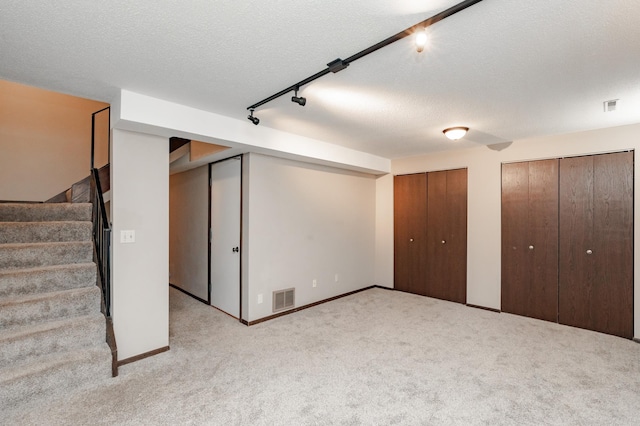 basement featuring light colored carpet, a textured ceiling, and rail lighting