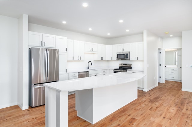 kitchen with appliances with stainless steel finishes, white cabinetry, sink, a center island, and light hardwood / wood-style floors