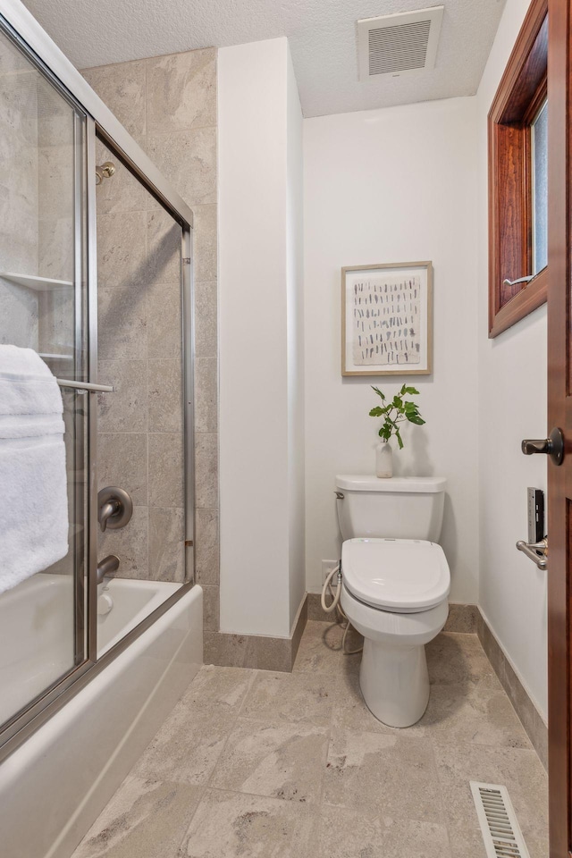 bathroom featuring toilet and shower / bath combination with glass door