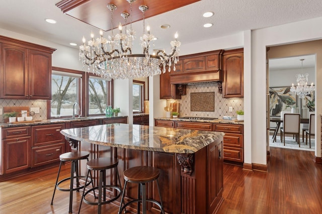 kitchen with stainless steel gas cooktop, sink, decorative light fixtures, a chandelier, and a center island