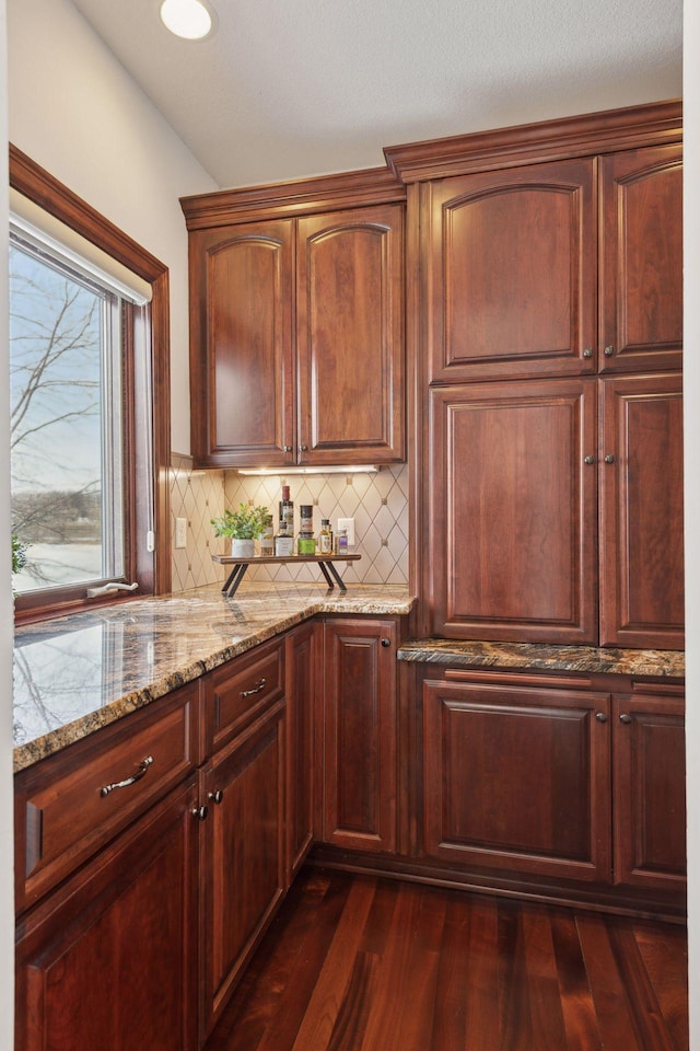 kitchen with light stone countertops, dark wood-type flooring, and decorative backsplash