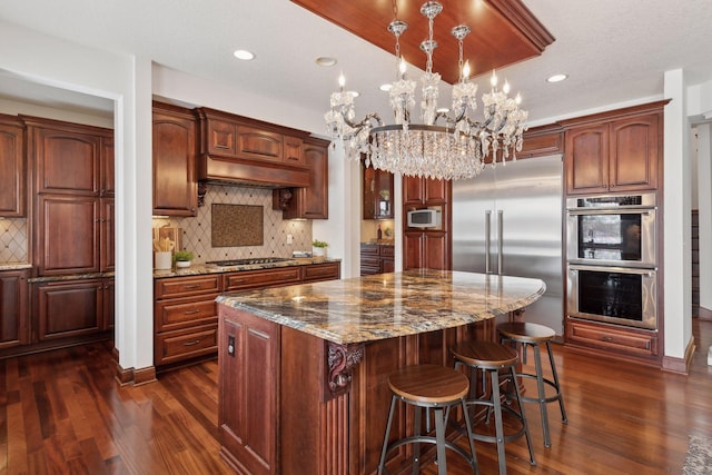 kitchen with built in appliances, decorative light fixtures, tasteful backsplash, and a center island