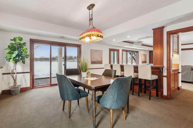 dining area with a water view, carpet flooring, a textured ceiling, and a tray ceiling