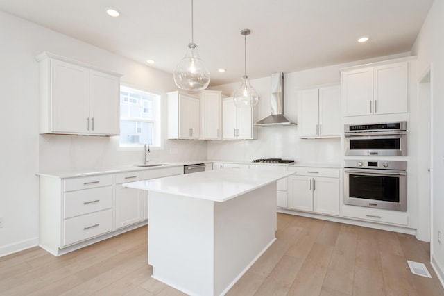 kitchen with appliances with stainless steel finishes, a center island, white cabinetry, wall chimney range hood, and hanging light fixtures