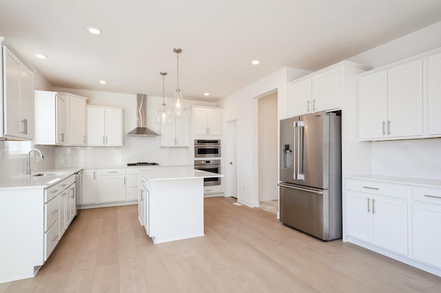 kitchen with a center island, wall chimney exhaust hood, decorative light fixtures, white cabinetry, and stainless steel appliances