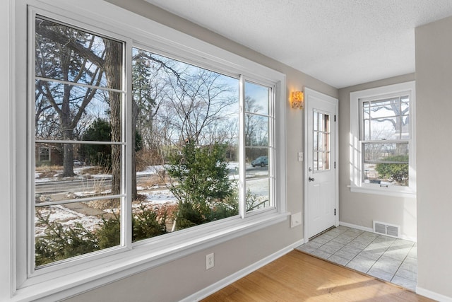 doorway to outside with plenty of natural light, a textured ceiling, and light wood-type flooring