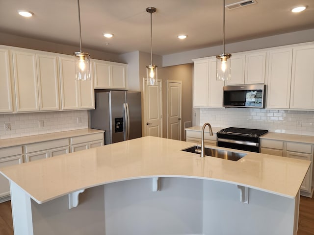 kitchen with a kitchen island with sink, sink, decorative light fixtures, and appliances with stainless steel finishes