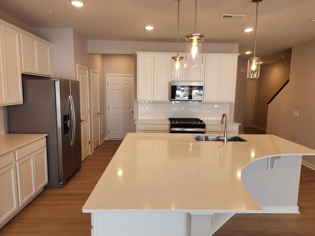 kitchen with sink, appliances with stainless steel finishes, hanging light fixtures, light stone counters, and a center island with sink