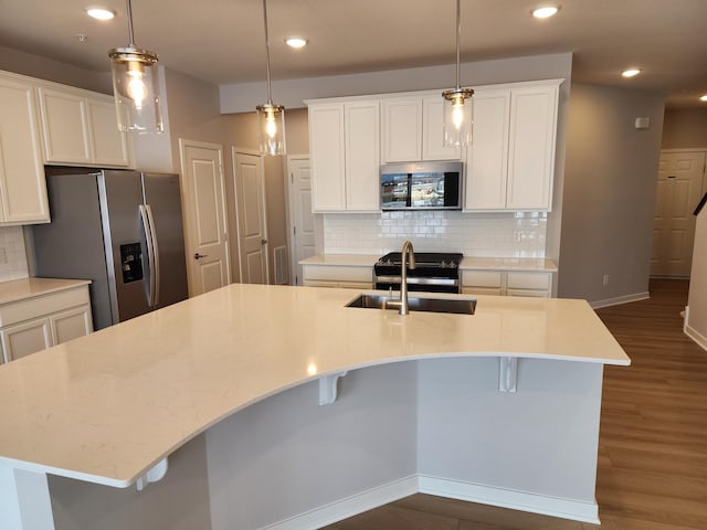 kitchen featuring tasteful backsplash, white cabinetry, hanging light fixtures, stainless steel appliances, and a center island with sink