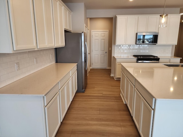 kitchen with appliances with stainless steel finishes, pendant lighting, white cabinetry, light stone countertops, and light wood-type flooring