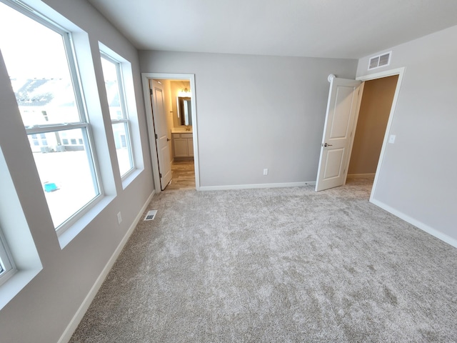 unfurnished bedroom featuring multiple windows, ensuite bathroom, and light colored carpet