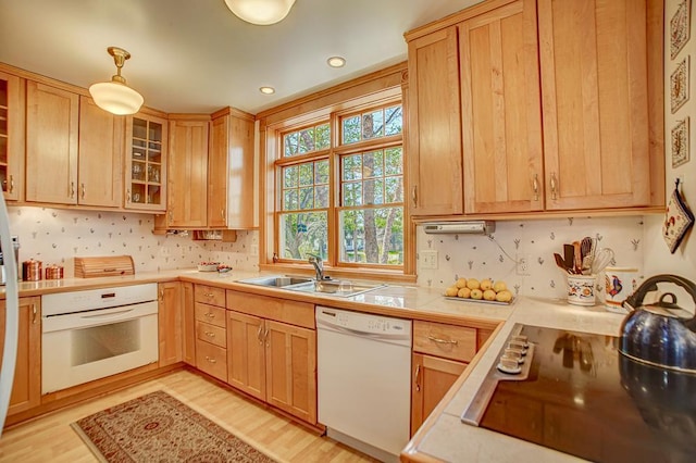 kitchen with white appliances, light brown cabinetry, a sink, and light countertops