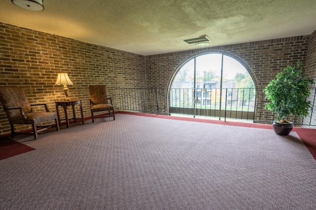 unfurnished room with a textured ceiling, carpet floors, and brick wall