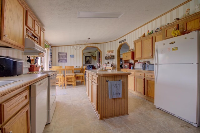 kitchen featuring light brown cabinetry, white appliances, a textured ceiling, and a kitchen island