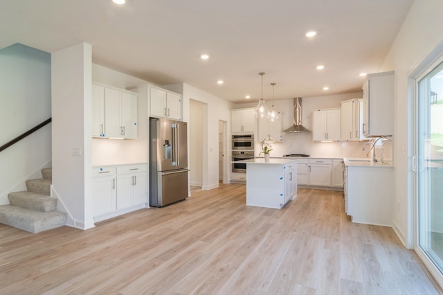 kitchen featuring pendant lighting, a center island, white cabinetry, appliances with stainless steel finishes, and wall chimney exhaust hood