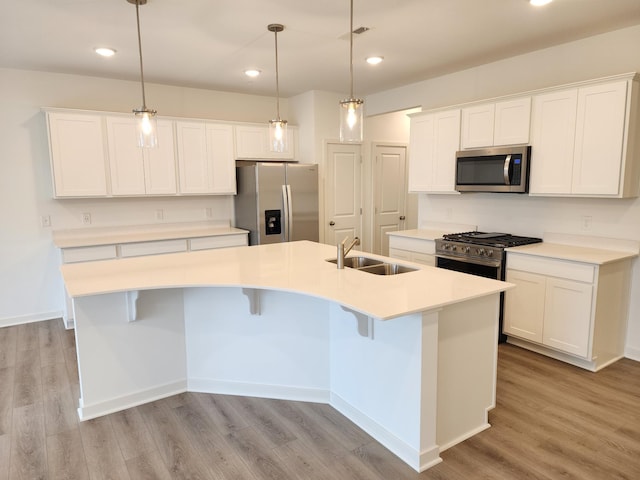 kitchen with pendant lighting, white cabinetry, stainless steel appliances, a center island with sink, and light wood-type flooring