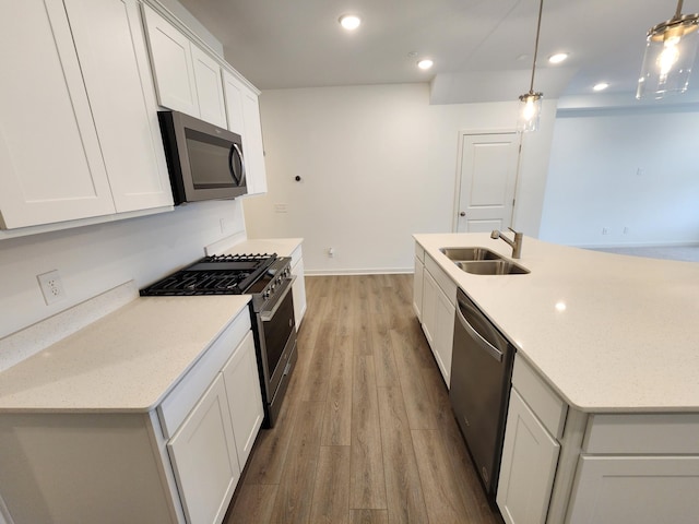 kitchen with appliances with stainless steel finishes, white cabinetry, sink, hanging light fixtures, and light hardwood / wood-style flooring