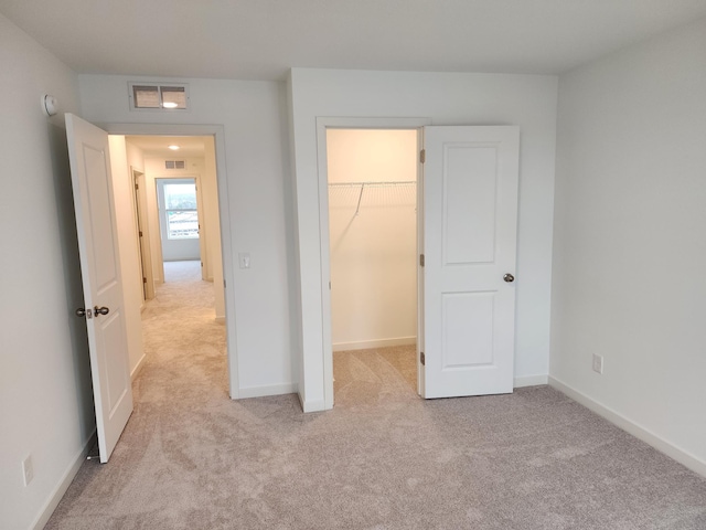 unfurnished bedroom with a walk in closet, light colored carpet, and a closet