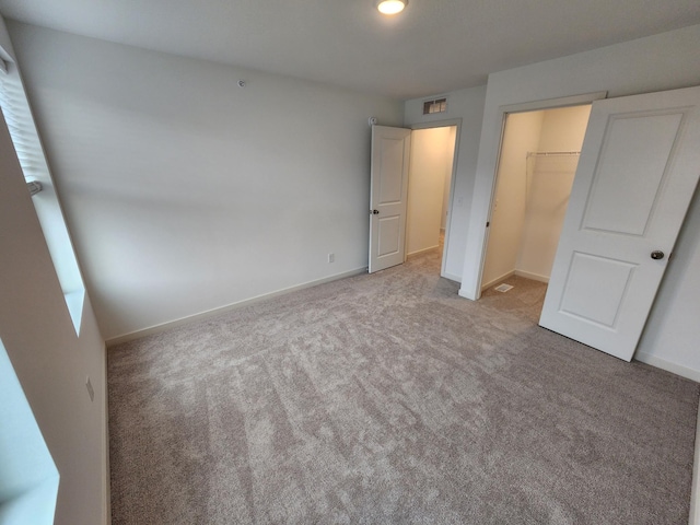 unfurnished bedroom with a walk in closet, light colored carpet, and a closet