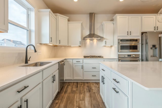 kitchen with hardwood / wood-style floors, sink, white cabinets, stainless steel appliances, and wall chimney exhaust hood