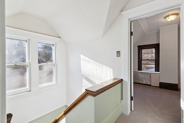 hallway featuring lofted ceiling, carpet floors, and a textured ceiling